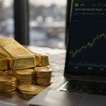 Gold bars and coins next to a laptop showing an ETF stock chart, comparing physical gold and gold ETF investing